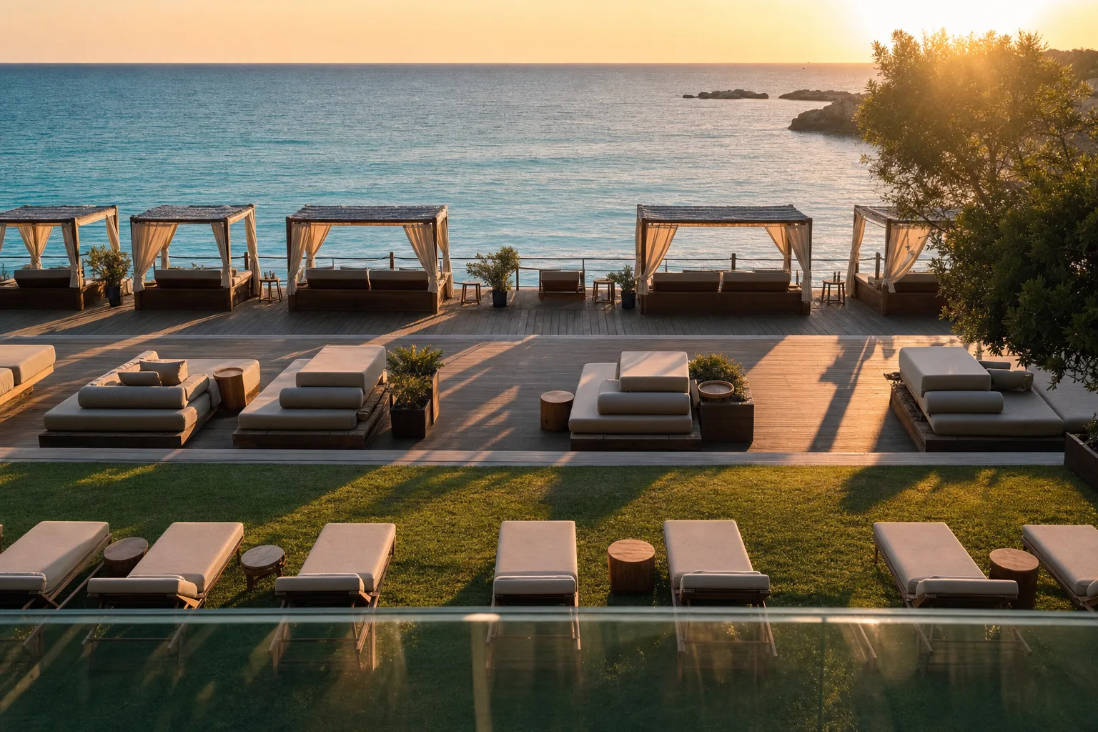 Tiered beach club seating at golden hour, cabanas at the waterline, daybeds mid-deck and sunbeds on the lawn