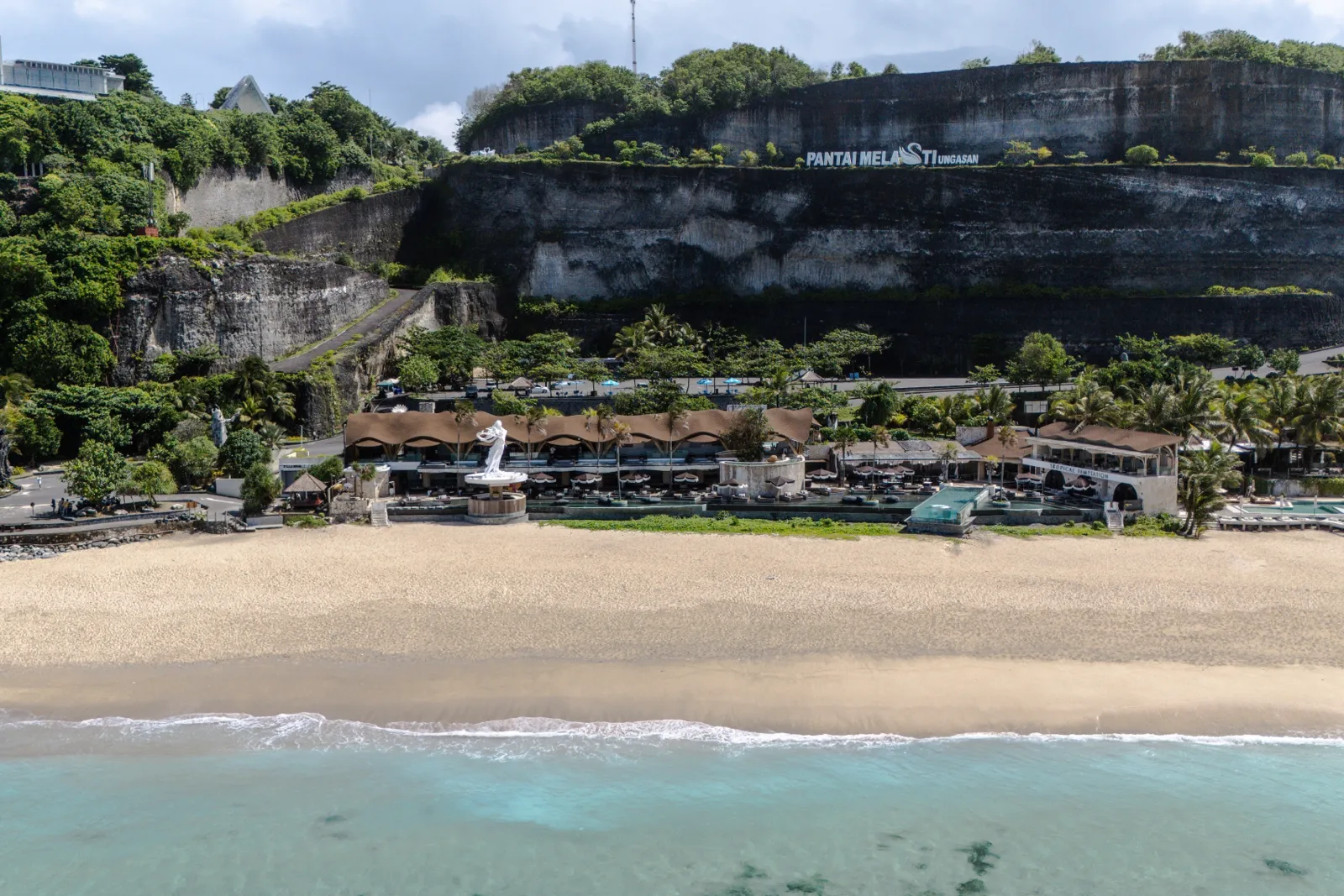 Aerial view of Tropical Temptation Beach Club on Melasti Beach, Bali: the beach club, pools and sand below the limestone cliffs